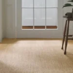 A bright, minimal hallway featuring a natural, golden-toned sisal carpet with a subtle woven pattern